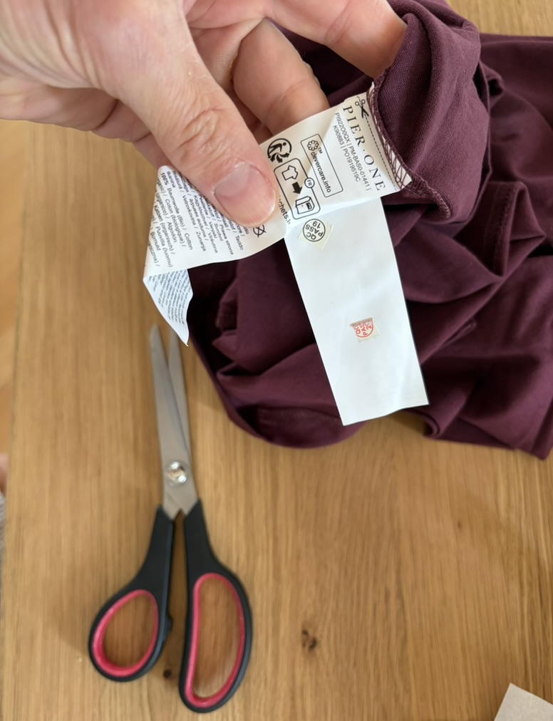 Several long clothing labels being cut from a burgundy garment